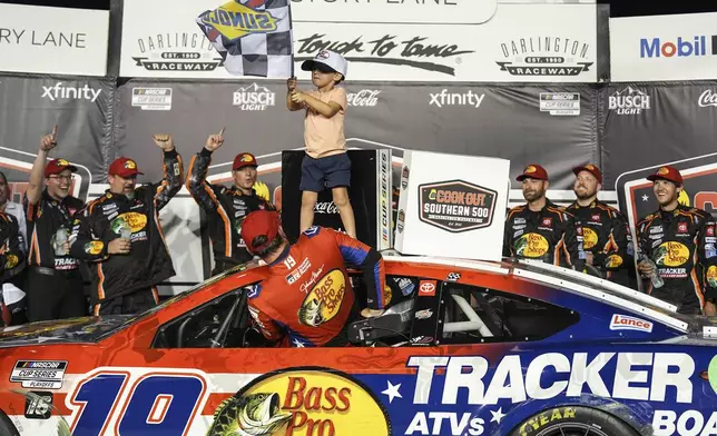 Chase Briscoe (19) climbs out of his car as his son Brooks, top, waves the checked flag in Victory Lane after winning a NASCAR Cup Series auto race at Darlington Raceway, Sunday, Aug. 31, 2025, in Darlington, S.C. (AP Photo/Matt Kelley)