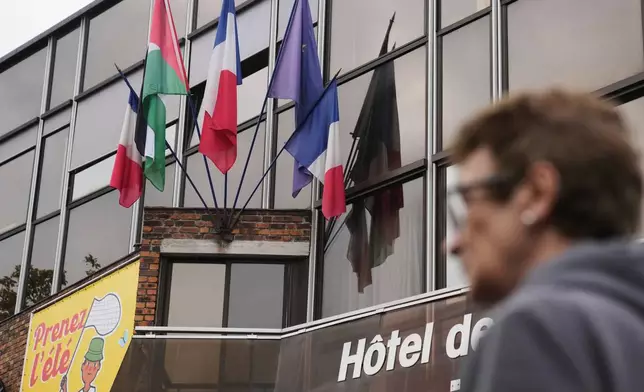 A woman walks past a Palestinian flag set up between French and European flags at the Malakoff's town hall, outside Paris, as France prepares to formally recognize a Palestinian state at the United Nations General Assembly, Sunday, Sept. 21, 2025.(AP Photo/Christophe Ena)