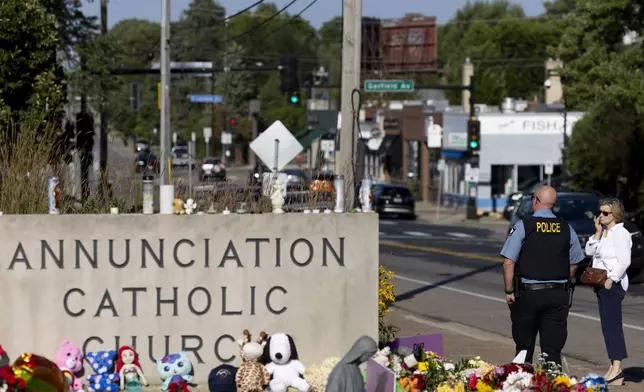 A police officer passes a mourner outside Annunciation Catholic Church after Wednesday's shooting at the school, Sunday, Aug. 31, 2025, in Minneapolis. (AP Photo/Ellen Schmidt)