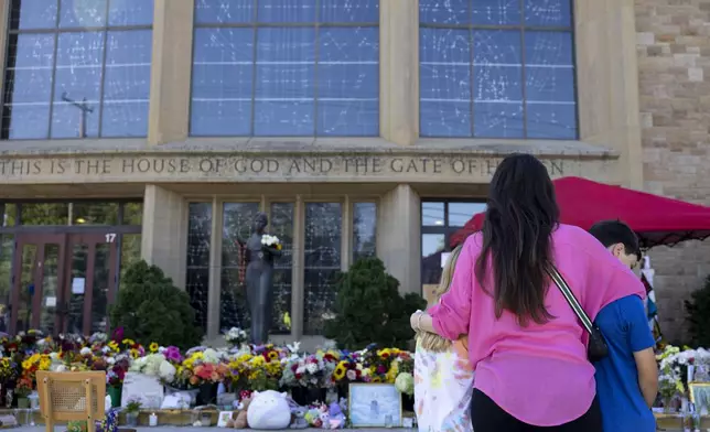 A mother holds her children at the memorial outside Annunciation Catholic Church after Wednesday's shooting, Sunday, Aug. 31, 2025, in Minneapolis.(AP Photo/Ellen Schmidt)