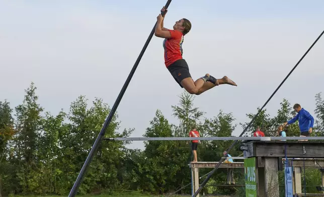 A female jumps towards the carbon pole to cross a body of water during a Fierljeppen competition in Kockengen, Netherlands, Wednesday, Aug. 27, 2025. (AP Photo/Peter Dejong)