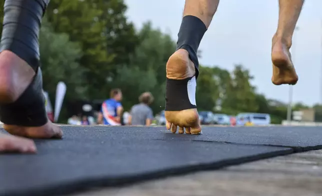 An athlete, wearing a rubber band on his foot to climb the pole, runs towards a long pole to jump across a body of water during a Fierljeppen competition in Kockengen, Netherlands, Wednesday, Aug. 27, 2025. (AP Photo/Peter Dejong)