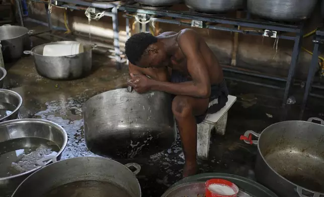 A man cleans pots at a makeshift shelter for people displaced by gang violence in Port-au-Prince, Haiti, Wednesday, Sept. 17, 2025. (AP Photo/Odelyn Joseph)