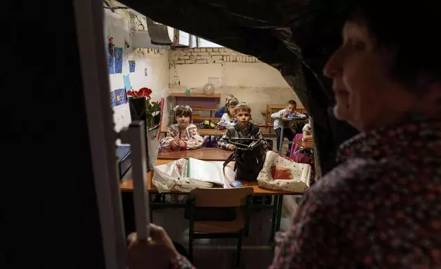 School students listen to their teacher during a lesson, in the basement of a municipal building during the first day in school in Bobryk, Sumy region, Ukraine, Monday, Sept. 1, 2025. The Bobryk school was forced to move to the basement due to endless alarms. (AP Photo/Evgeniy Maloletka)
