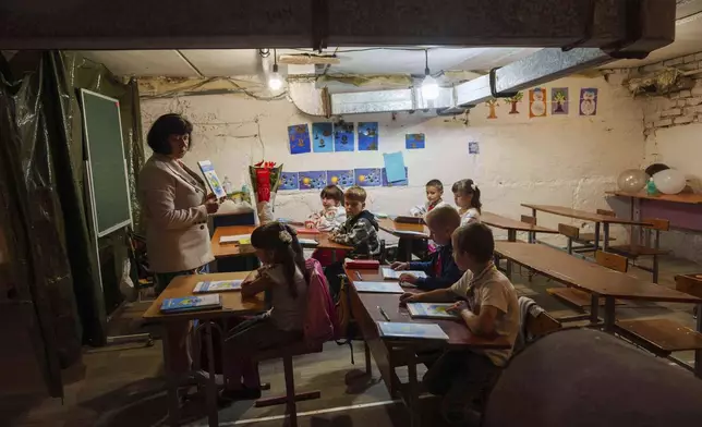 School students listen to their teacher during a lesson, in the basement of a municipal building during the first day in school in Bobryk, Sumy region, Ukraine, Monday, Sept. 1, 2025. The Bobryk school was forced to move to the basement due to endless alarms. (AP Photo/Evgeniy Maloletka)