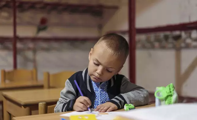 A school boy draws during a lesson, in the basement of a municipal building during the first day in school in Bobryk, Sumy region, Ukraine, Monday, Sept. 1, 2025. The Bobryk school was forced to move to the basement due to endless alarms. (AP Photo/Evgeniy Maloletka)