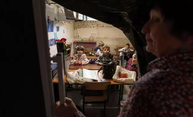 School students listen to their teacher during a lesson, in the basement of a municipal building during the first day in school in Bobryk, Sumy region, Ukraine, Monday, Sept. 1, 2025. The Bobryk school was forced to move to the basement due to endless alarms. (AP Photo/Evgeniy Maloletka)