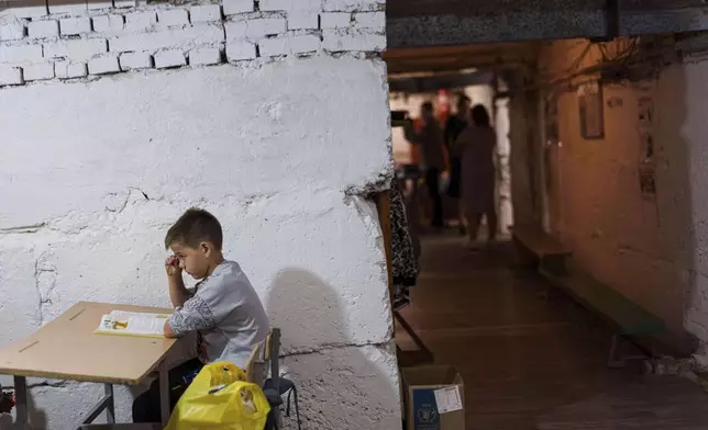 A school boy listens to a teacher during a lesson, in the basement of a municipal building during the first day in school in Bobryk, Sumy region, Ukraine, Monday, Sept. 1, 2025. The Bobryk school was forced to move to the basement due to endless alarms. (AP Photo/Evgeniy Maloletka)