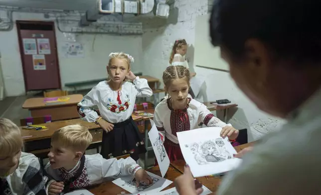 School students listen to their teacher during a lesson, in the basement of a municipal building during the first day in school in Bobryk, Sumy region, Ukraine, Monday, Sept. 1, 2025. The Bobryk school was forced to move to the basement due to endless alarms. (AP Photo/Evgeniy Maloletka)