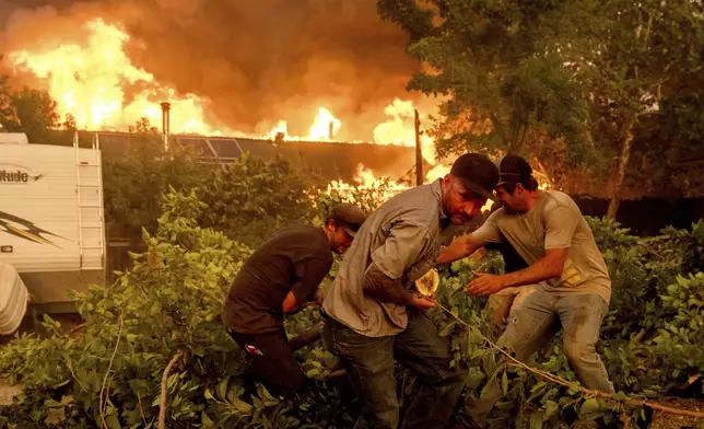 Residents work to stop flames from a burning home from spreading to a neighboring house as the 6-5 Fire burns through the Chinese Camp community of Tuolumne County, Calif., on Tuesday, Sept. 2, 2025. (AP Photo/Noah Berger)