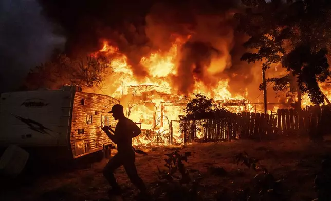 A residents works to stop flames from a burning home from spreading to a neighboring house as the 6-5 Fire burns through the Chinese Camp community of Tuolumne County, Calif., on Tuesday, Sept. 2, 2025. (AP Photo/Noah Berger)