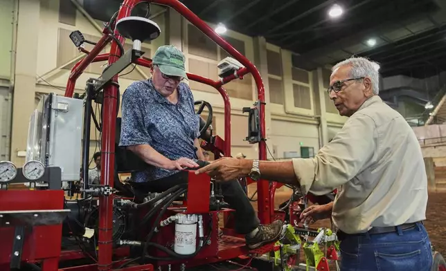 Farmer Vicki Morrane, left, listens as Ajit Srivastava, right, explains the mechanics of an electric tractor before she test drives Tuesday, Aug. 19, 2025, in East Lansing, Mich. (AP Photo/Joshua A. Bickel)
