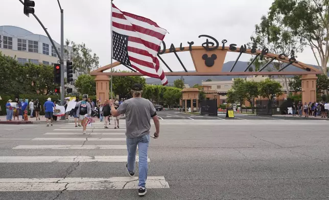 A U.S. flag is carried across a street in front of a demonstration in response to the suspension of Jimmy Kimmel's late-night show outside of Walt Disney Studios in Burbank, Calif., on Thursday, Sept. 18, 2025. (AP Photo/Jae C. Hong)
