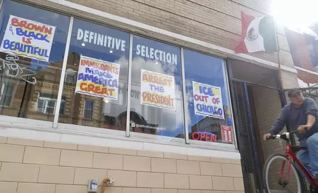 A bicyclist passes Definitive Selection clothing store, one of many businesses in the predominantly Latino neighborhood that has seen a slowdown in foot traffic since President Donald Trump's threats of a federal law enforcement intervention, on Friday, Sept. 5, 2025 in Chicago. (AP Photo/Mark Vancleave)