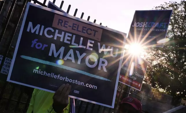 Sunrise peeks through campaign signs of Boston Mayor Michelle Wu and challenger Josh Kraft at a polling place, Tuesday, Sept. 9, 2025, in the Roslindale neighborhood of Boston. (AP Photo/Charles Krupa)