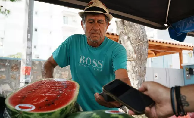 Fruit vendor Makis Panaretos uses a POS terminal for a customer who pays with his cellphone at an open-air fruit and vegetable market in Athens, Greece, Friday, Sept. 5, 2025. (AP Photo/Thanassis Stavrakis)