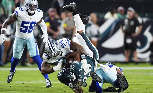 Philadelphia Eagles running back Saquon Barkley (26) is stopped after a gain by Dallas Cowboys' Sam Williams, top, and Malik Hooker, bottom, in the first half of an NFL football game Thursday, Sept. 4, 2025, in Philadelphia.(AP Photo/Chris Szagola)