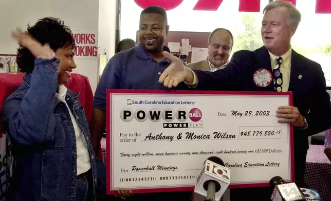FILE - South Carolina Education Lottery Director, Ernie Passailaigue , right, extends his hand to Monica and Anthony Wilson, of Charlotte, N.C., as he presents them with a check for their Powerball winnings Thursday May 29, 2003, at Red Rocket Fireworks in Fort Mill, S.C. (AP Photo/Mary Ann Chastain, File)