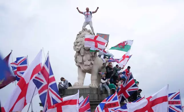 A demonstrator stands on the head of the South Bank lion that sits on the side of the Westminster Bridge, during a Tommy Robinson-led Unite the Kingdom march and rally in London, Saturday, Sept. 13, 2025. (AP Photo/Joanna Chan)