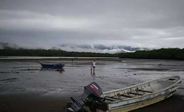Venezuelan Abraham Castro and his partner's son Mathias Gomez walk on the beach in Jaque on Panama's Pacific coast, from where they will keep moving south toward Colombia, Friday, Sept. 19, 2025. Castro, his partner, and her two sons are returning home after being detained by U.S. authorities in Texas and sent back to southern Mexico. (AP Photo/Matias Delacroix)