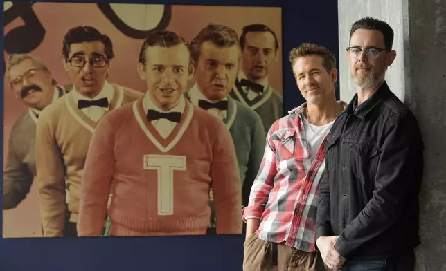 Colin Hanks, right, director of the documentary film "John Candy: I Like Me," poses for a portrait with producer Ryan Reynolds in front of a photograph of Second City comedy performers including John Candy, far left, to promote the film during the Toronto International Film Festival on Thursday, Sept. 4, 2025, in Toronto. (AP Photo/Chris Pizzello)