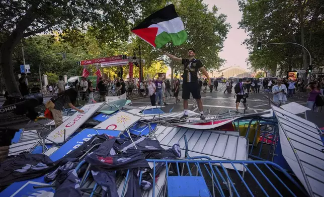A protester waves a Palestinian flag on top of fences used as barricades to block the street to disrupt the twenty-first stage of the Spanish cycling race La Vuelta, from Alalpardo to Madrid, Spain, Sunday, Sept. 14, 2025. (AP Photo/Manu Fernández)