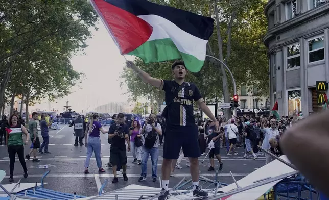 A protester waves a Palestinian flag on top of fences used as barricades to block the street trying to disrupt the twenty-first stage of the Spanish cycling race La Vuelta, from Alalpardo to Madrid, Spain, Sunday, Sept. 14, 2025. (AP Photo/Andrea Comas)