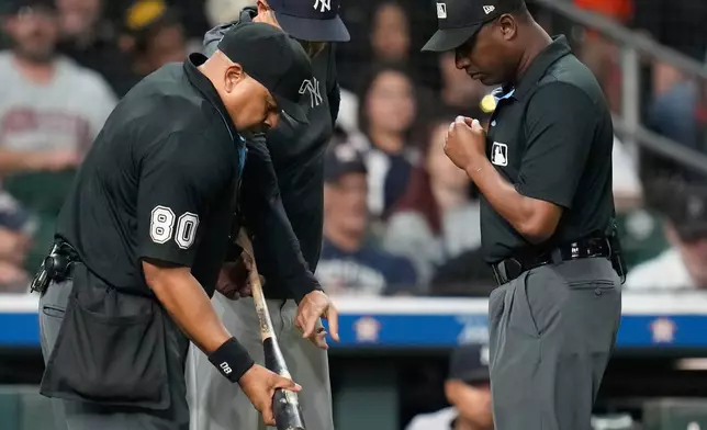 New York Yankees manager Aaron Boone, center, points at Houston Astros' Taylor Trammell's bat held home plate umpire Adrian Johnson, left, as umpire Ramon De Jesus, right, looks on during the ninth inning of a baseball game Thursday, Sept. 4, 2025, in Houston. (AP Photo/Karen Warren)