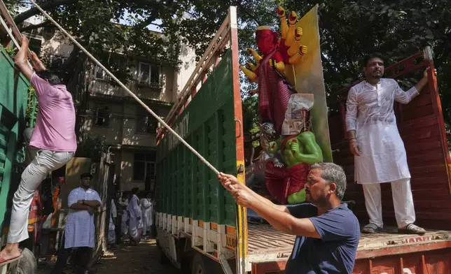 Workers use ropes to secure an idol of the Hindu goddess Durga on a truck as it is transported to a place of worship ahead of the Durga Puja festival in New Delhi, India, Sunday, Sept. 21, 2025. (AP Photo/Manish Swarup)