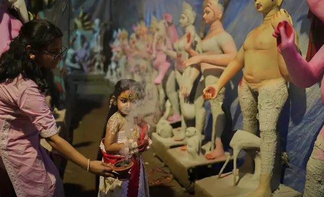 A woman uses smoke as a prop to photograph her child, who is dressed as the Hindu goddess Durga, at a temporary shelter where idols of Hindu gods and goddesses are being made ahead of the Durga Puja festival, in New Delhi, India, Friday, Sept. 19, 2025. (AP Photo/Manish Swarup)