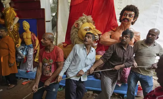 Workers pull ropes tied to the base of an idol of Durga as they move it onto a truck for transportation to a place of worship ahead of the Durga Puja festival in New Delhi, India, Sunday, Sept. 21, 2025. (AP Photo/Manish Swarup)