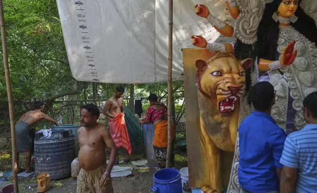 Workers and artists bathe while visitors look at an idol of the Hindu goddess Durga, which was created ahead of the Durga Puja festival in New Delhi, India, Saturday, Sept. 20, 2025. (AP Photo/Manish Swarup)