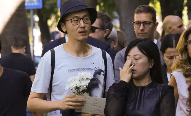 A man carrying flowers and a note addressed in Italian and Mandarin to the family of "Signor Giorgio Armani" waits in line to pay his respects to fashion designer Giorgio Armani, lying in state at the Armani/Teatro in Milan, northern Italy, Saturday, Sept. 6, 2025. (AP Photo/Antonio Calanni)
