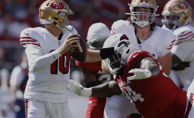 San Francisco 49ers quarterback Mac Jones, left, avoids a tackle by Arizona Cardinals defensive end Dalvin Tomlinson during the second half of an NFL football game Sunday, Sept. 21, 2025, in Santa Clara, Calif. (AP Photo/Sergio Estrada)