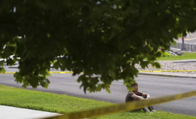 A person sits near crime scene tape near a memorial after Turning Point USA CEO and co-founder Charlie Kirk was shot and killed at Utah Valley University, Saturday, Sept. 13, 2025, in Orem, Utah. (AP Photo/Lindsey Wasson)