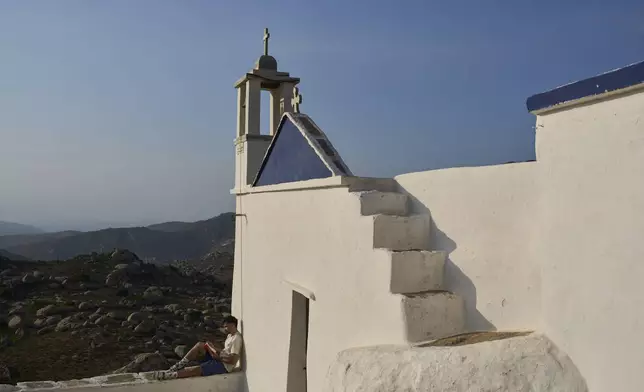 Giannis Kafantaris 26, reads a book outside Panagia Theoskespasti, the chapel his family co-owns near the village of Falatados, on the Aegean island of Tinos, Greece, Friday, Sept. 5, 2025. (AP Photo/Petros Giannakouris)