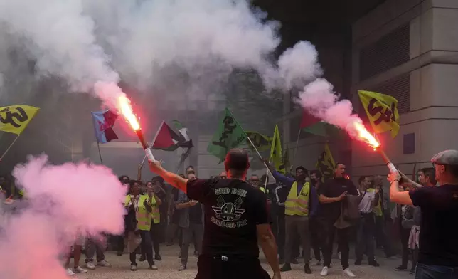 Striking rail workers wave flares into the Paris headquarters of the Economics Ministry during a protest called by major trade unions to oppose budget cuts, in Paris, France, Thursday, Sept. 18, 2025. (AP Photo/Michel Euler)