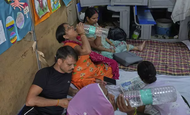 Bindu Pandey, center, drinks water after reaching in a temporary school shelter, which houses residents displaced from the banks of the Yamuna River by incessant rain in the higher regions in New Delhi, India, Friday, Sept. 5, 2025. (AP Photo/Manish Swarup)