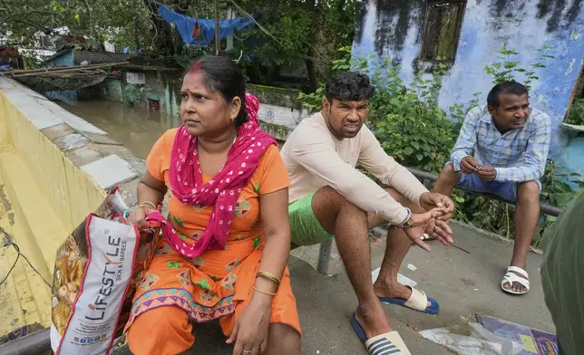 Bindu Pandey, 40, left, sits on the wall near the floodwaters of the swollen Yamuna River, leaving behind her inundated home on the banks to seek refuge in a temporary shelter, in New Delhi, India, Friday, Sept. 5, 2025. (AP Photo/Manish Swarup)