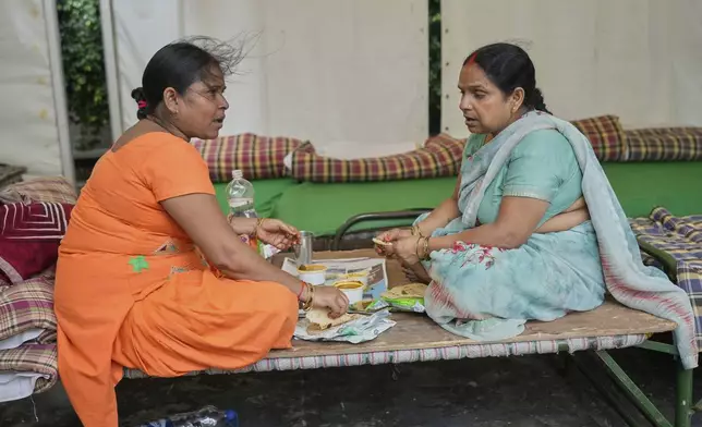 Bindu Pandey, left, eats lunch with her relative in a temporary school shelter, which houses residents displaced from the banks of the Yamuna River by incessant rain in the higher regions, in New Delhi, India, Friday, Sept. 5, 2025. (AP Photo/Manish Swarup)