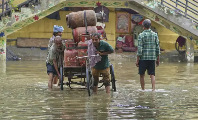 People help a rickshaw driver carrying gas cylinders to cross flooded water after the river Yamuna, swollen by incessant rain in the higher regions, overran its banks, in New Delhi, India, Friday, Sept. 5, 2025. (AP Photo/Manish Swarup)