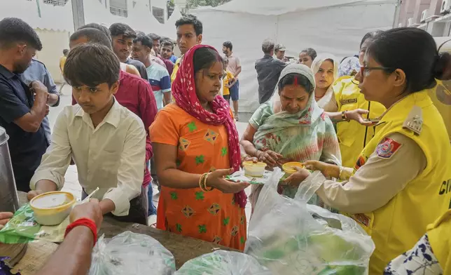 Bindu Pandey, center, takes food in a temporary school shelter, which houses residents displaced from the banks of the Yamuna River by incessant rain in the higher regions in New Delhi, India, Friday, Sept. 5, 2025. (AP Photo/Manish Swarup)