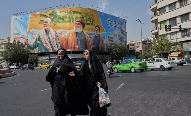 Two women walk past a huge banner showing the late commander of the Iran's Revolutionary Guard expeditionary Quds Force, Gen. Qassem Soleimani, who was killed in a U.S. drone attack in 2020, and two late Hezbollah leaders Hassan Nasrallah, center, and Hashem Safieddine, who were killed in Israeli airstrikes in 2024, at the Enqelab-e-Eslami (Islamic Revolution) square, in Tehran, Iran, Saturday, Sept. 27, 2025. (AP Photo/Vahid Salemi)
