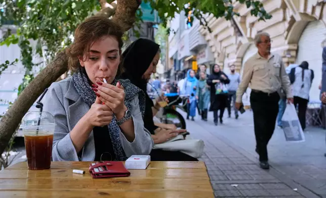 A woman lights a cigarette in the alfresco dining area of a cafe at the Enqelab-e-Eslami (Islamic Revolution) street, in Tehran, Iran, Saturday, Sept. 27, 2025. (AP Photo/Vahid Salemi)