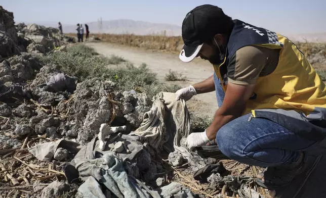 A Syrian Civil Defense worker checks clothes found along with human remains in Otaiba, on the outskirts of Damascus, Syria, Friday, Sept. 19, 2025. (AP Photo/Omar Albam)