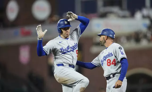 Los Angeles Dodgers' Freddie Freeman, left, celebrates with first base coach Chris Woodward after hitting a single during the fifth inning of a baseball game against the San Francisco Giants, Saturday, Sept. 13, 2025, in San Francisco. (AP Photo/Godofredo A. Vásquez)