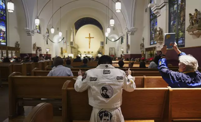 Parishioner of the Blessed Carlo Acutis Parish, Kelly Legamaro, center, prays during Mass while wearing an outfit showing the face of Acutis, who will be canonized a saint by Pope Leo XIV, on Wednesday, Sept. 3, 2025, in Chicago. (AP Photo/Jessie Wardarski)