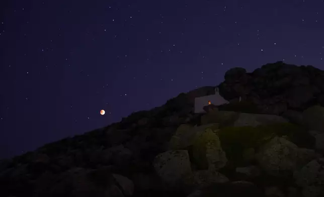 The moon glows red during a total lunar eclipse above the chapel of Panagia Skepasti near Volax village, on the island of Tinos, Greece, Sunday, Sept. 7, 2025. (AP Photo/Petros Giannakouris)