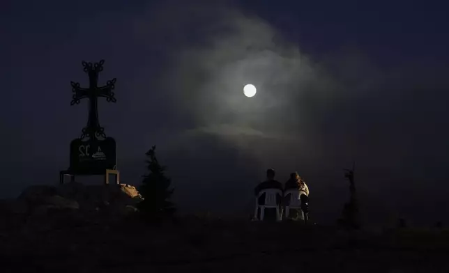 A Lebanese couple watch as the moon shines during a total lunar eclipse over Kfardebian village, northeast of Beirut, Lebanon, Sunday, Sept. 7, 2025. (AP Photo/Bilal Hussein)