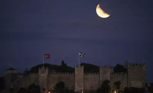 The full moon, still half obscured by the Earth's shadow after a full eclipse, rises behind the Saint George's Castle in Lisbon, Sunday, Sept. 7, 2025. (AP Photo/Armando Franca)